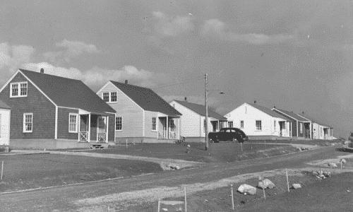 Black and white picture of single homes with a vehicle in the driveway of one of the homes