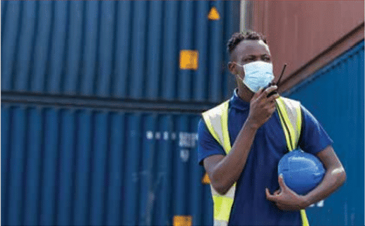 Man wearing face mask talking on walkie-talkie with shipping containers in background